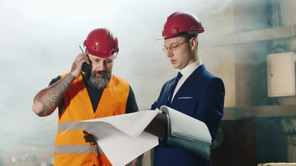 Lagarbete av byggare och ingenjörskonst. Byggnadsarbetare prata i radio, ingenjör studera ritningar — Stockvideo