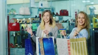 İki arkadaş eğlenceli alışveriş torbaları ile dans. Depodaki cam vitrinler arka planı