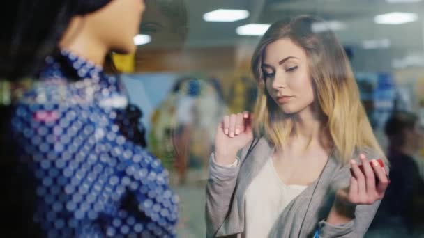 Mujer atractiva joven contempla escaparate tienda de ropa. En las manos en su tarjeta para ir de compras y bolsas de compras — Vídeos de Stock