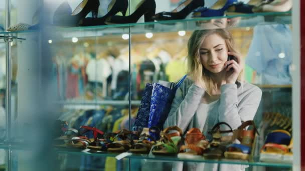 Attractive woman talking on the phone in the glass showcases shoe store — Stock Video