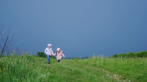 Dos niñas corriendo por un camino rural. Sobre el fondo de un cielo tormentoso y la lluvia que se acerca — Vídeos de Stock