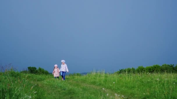 Twee meisjes op een landelijke weg richting de camera uitgevoerd. Tegen de achtergrond van een stormachtige lucht, slow-motion video — Stockvideo