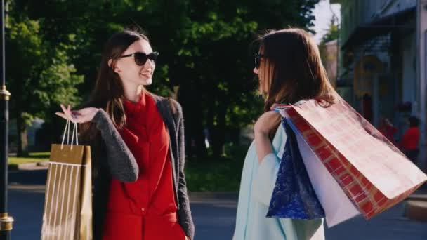 Dos mujeres hablan con entusiasmo de sus compras. En las manos sosteniendo bolsas de compras — Vídeos de Stock