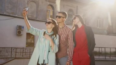Arkadaşlar iki kadın ve bir adam güneşte selfie yapıyor. Eski bir binanın arka planında