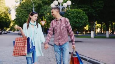 Alışveriş torbalarıyla şehirde yürüyen genç bir çift. Mutlular, gülümsüyorlar, konuşuyorlar.