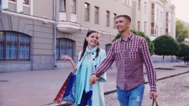 Alışveriş çantalarıyla şehirde yürüyen bir adam ve bir kadın..