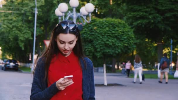 Aantrekkelijke vrouw die door de straat loopt, genietend van een smartphone — Stockvideo