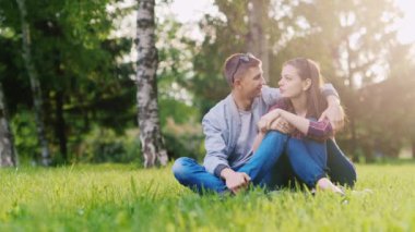 Genç çekici çift rahatlatıcı sarılma, gülümseyen parkta.