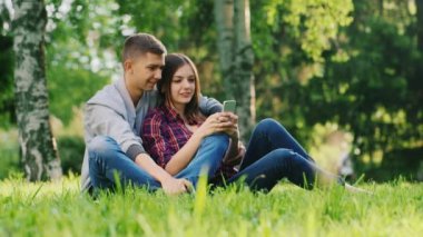 Genç çift birlikte parkta, dinlenme oyun üstünde senin telefon, gülümseyen.