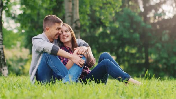 Young attractive couple relaxing in nature. Sitting on the grass, hugging, smiling, laughing — Stock Video