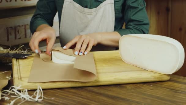 Mãos de vendedor um pedaço de queijo são embalados em embalagens de papel — Vídeo de Stock
