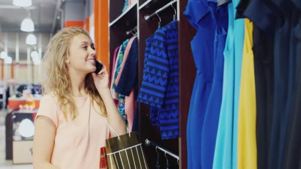 Mujer joven camina por el banco con ropa, hablando por teléfono — Vídeos de Stock