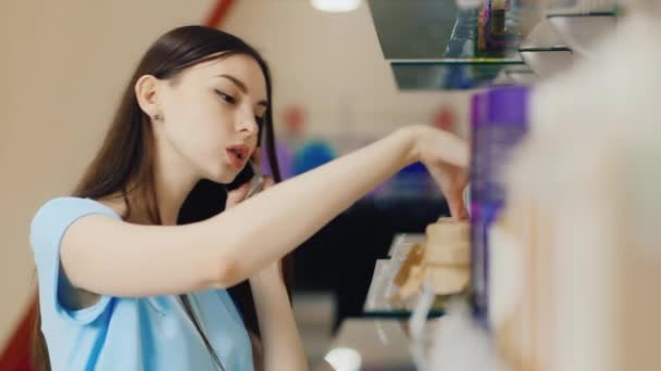 Jovem escolhe itens no departamento de perfumes, falando ao telefone — Vídeo de Stock