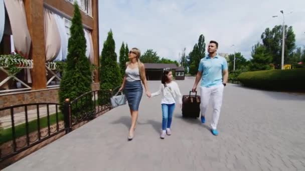 Steadicam shot: Famiglia felice - mamma papà e figlia arrivano con una borsa da viaggio in hotel. Famiglia in arrivo in vacanza — Video Stock