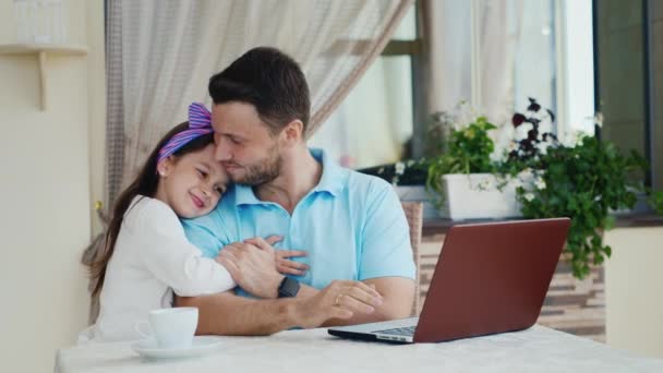 Um homem jovem e bonito de férias. Mostra a sua filha algo em um laptop, este é o terraço de verão no café — Vídeo de Stock