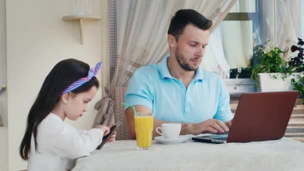 Un uomo che lavora su un computer portatile con lui ragazza di 6 anni utilizzando un telefono cellulare — Video Stock