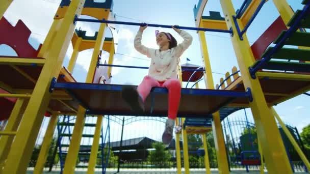 Girl playing on the playground. Laughter, fun, sunshine in her hair. He is sitting and looking at the camera — Stock Video