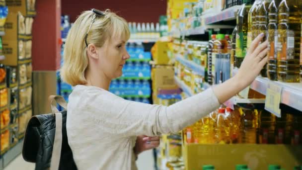 Молода жінка дивиться на пляшку оливкової або іншої олії в супермаркеті — стокове відео