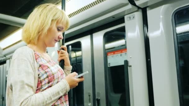 En ung kvinna läser ett meddelande på telefonen, gå till tunnelbanan. Stående nära dörren vagnen — Stockvideo