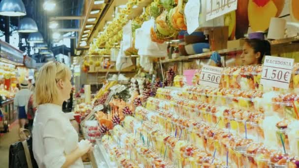 Barcelona, Spanien - 15 juni 2016: Kvinna turist tittar på ett stort skyltfönster med godis och blommor. Den berömda la Boqueria-marknaden — Stockvideo