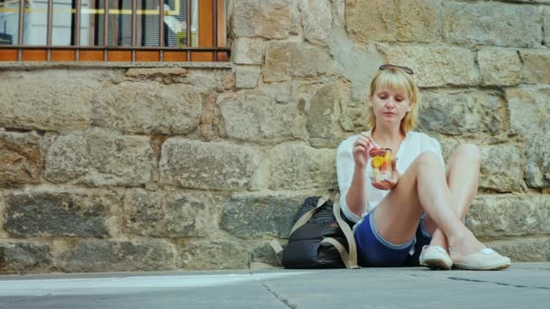 Kvinnan turist sitter på den gamla byggnaden, äta frukt från koppen. Barcelonas gotiska kvarter — Stockvideo