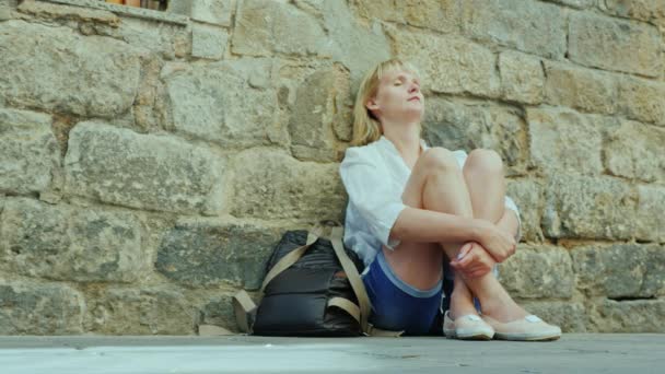 Tired woman sitting in an old building wall. Concept - get lost in an unfamiliar city — Stock Video