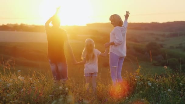 Mãe com dois filhos - uma menina e um menino felizes pulando e acenando com as mãos para o sol — Vídeo de Stock