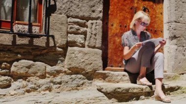 Rupit Köyü eski bir evde merdivenlerde oturan kadın turist. Kılavuzunu okuyun