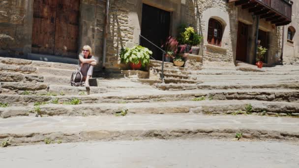 La mujer se sienta en los escalones de la antigua ciudad de Cataluña Rupit. Un lugar popular entre los turistas — Vídeos de Stock