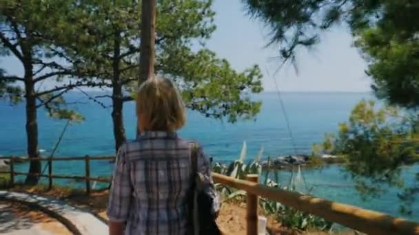 Steadicam Shot: A female tourist walks along the Mediterranean coast. Back view — Stock Video