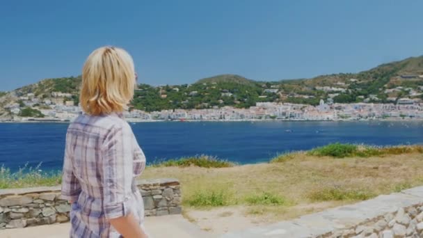 ステディカム撮影: 女性観光客がスペイン カダケスの地中海リゾートの背景に、海岸に沿って歩く — ストック動画