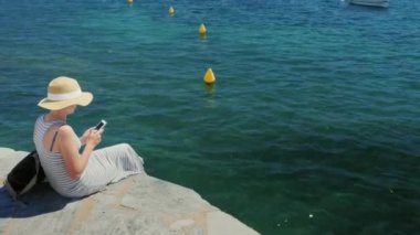 Vinç atış: kadın turist bir iskelede oturup yazmaya üstünde hareket eden telefon. Dünyanın herhangi bir yerinde bağlantı