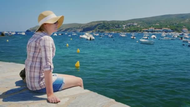 Frau sitzt am Strand und blickt auf den schönen Hafen mit Booten und Yachten — Stockvideo