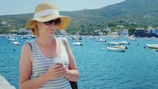 Steadicam shot: Una mujer camina a lo largo del paseo marítimo, escribiendo en el teléfono inteligente. La Costa Brava en España — Vídeo de stock