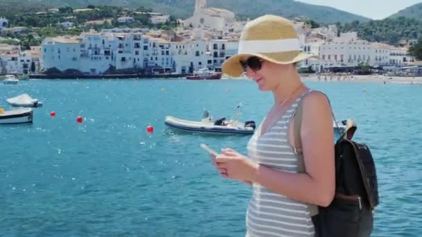 Een toerist met een wandeling langs de kade, rugzak te typen op de telefoon. Tegen de achtergrond van de baai met jachten — Stockvideo