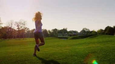 Steadicam yavaş vurdu: yeşil çimenlerin üzerinde çalışan güzel bir genç kadın.