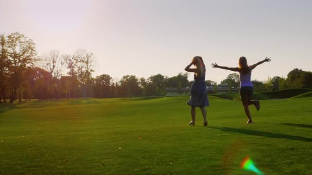 Steadicam shot: Two young girls having fun running on the green field towards the sun. Концепция - энергия, свобода, молодежь и здоровье — стоковое видео