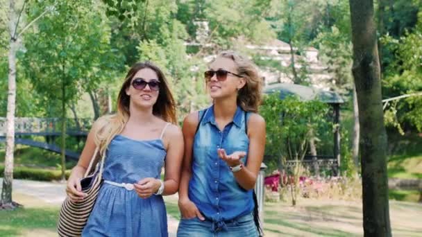 Steadicam shot: δύο γυναίκες φίλους που απολαμβάνουν μια βόλτα στο πάρκο, χαμογελαστός και γελά. Βίντεο αργής κίνησης — Αρχείο Βίντεο