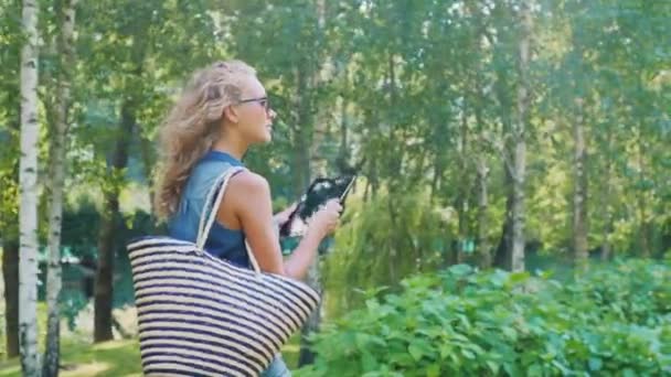 Jeune femme avec la tablette est dans le parc, vue arrière. Beau soleil avec des reflets dans le cadre — Video