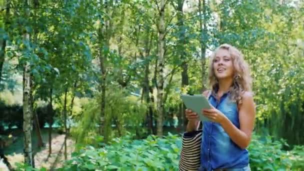 Приваблива жінка гуляє з табличкою в парку, дивлячись на карту — стокове відео