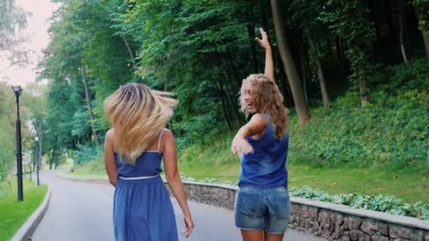 Two female friends having fun walking along the road, waving his arms, rejoicing walk. Back view — Stock Video