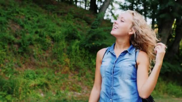Eine junge attraktive Frau spaziert durch den Wald, genießt den Spaziergang, lacht, glättet die Haare — Stockvideo
