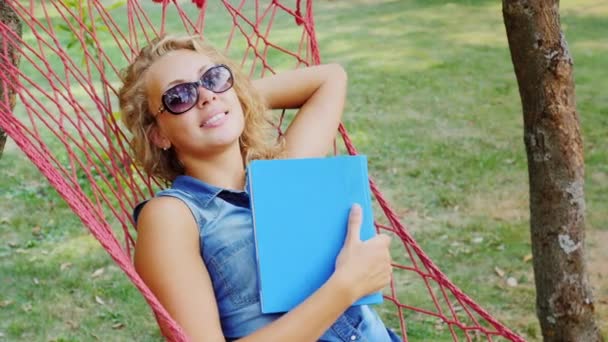 Jeune femme insouciante couchée dans un hamac et rêve. La main tenant un livre — Video