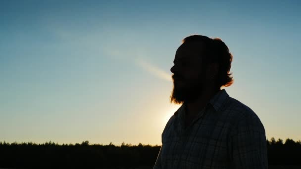 Sziluettjét a szakállas férfi, aki dohányzik a naplemente — Stock videók