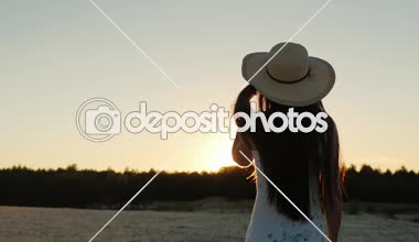 Atış Steadicam: şapkalı bir uzun saçlı genç kadın. Batan güneşin, arka görüş doğru git