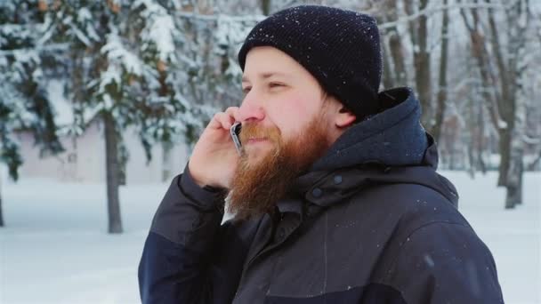 Aantrekkelijke jonge bebaarde man praten aan de telefoon. Het gaat in de winter park — Stockvideo