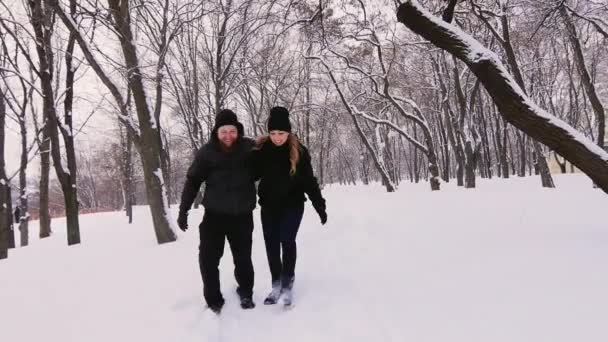 Um jovem casal se move para os bosques de inverno, seguindo um caminho estreito através da neve profunda — Vídeo de Stock