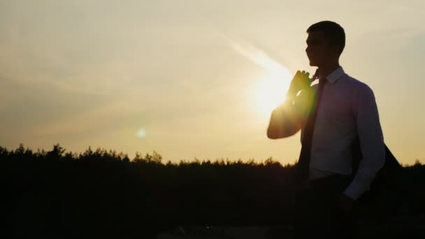 Joven hombre de negocios bien parecido en un traje de pie en una puesta de sol. Espera con confianza. Concepto: éxito, confianza, tranquilidad y fiabilidad — Vídeos de Stock