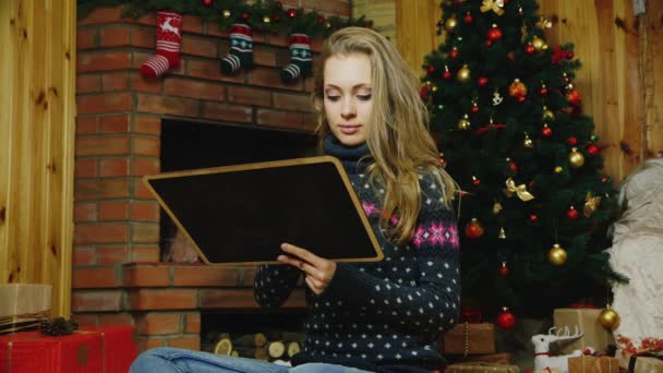 Una mujer atractiva con un signo de Año Nuevo 2017. Sentado junto a la chimenea cerca de las decoraciones de Navidad y calcetines para regalos — Vídeos de Stock