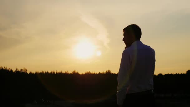 Silhouette of a young businessman talking on the phone. It stands on a sunset background. Back view — Stock Video